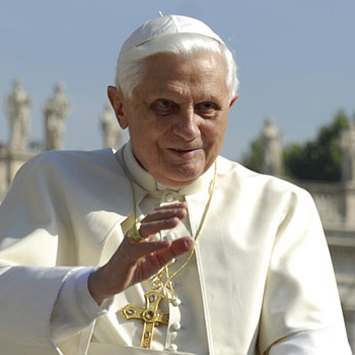 Papst Benedikt XVI begrüßt mit einer winkenden Hand und schaut freundlich